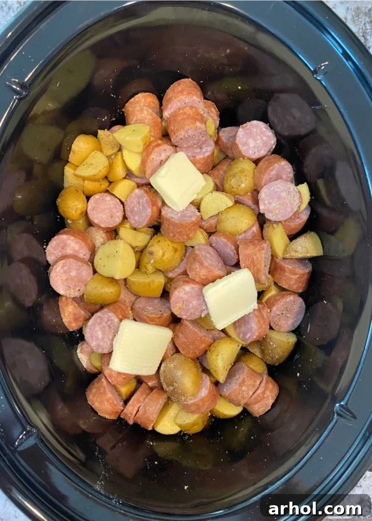 Smoked sausage, seasoned potatoes, and butter layered in the slow cooker, before cooking.