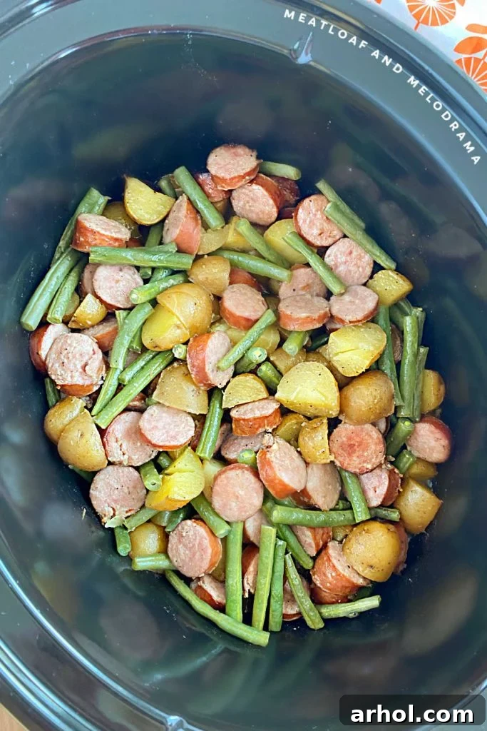 Cooked smoked sausage and potatoes with green beans in the slow cooker, steam rising from the delicious meal.