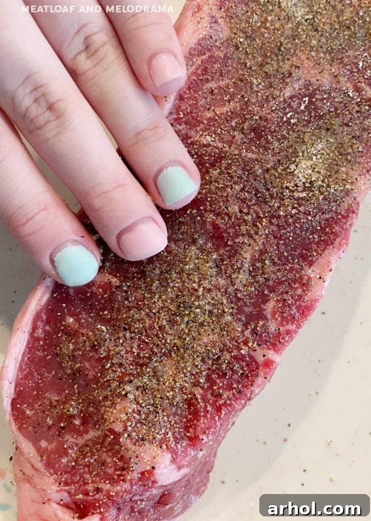 Applying seasoning blend to a New York strip steak with hands before grilling.