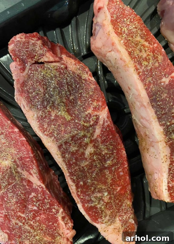 Placing seasoned New York strip steaks onto the preheated Ninja Foodi Grill XL with visible grill marks.