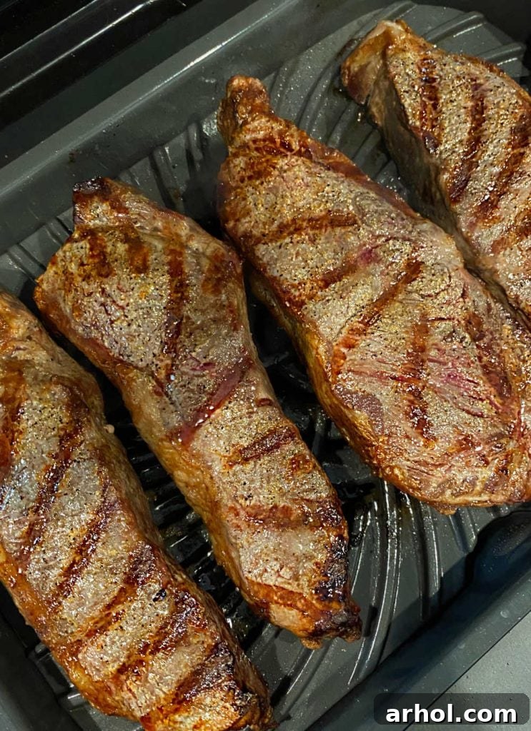 Grilled New York strip steaks with perfect grill marks cooking on an indoor Ninja Foodi Grill XL.