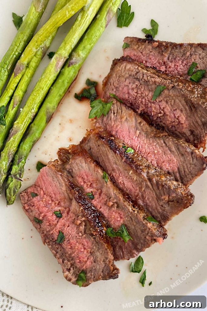Perfectly cooked medium New York strip steak, sliced and served with grilled asparagus on a white plate, prepared on a Ninja Foodi Grill XL.