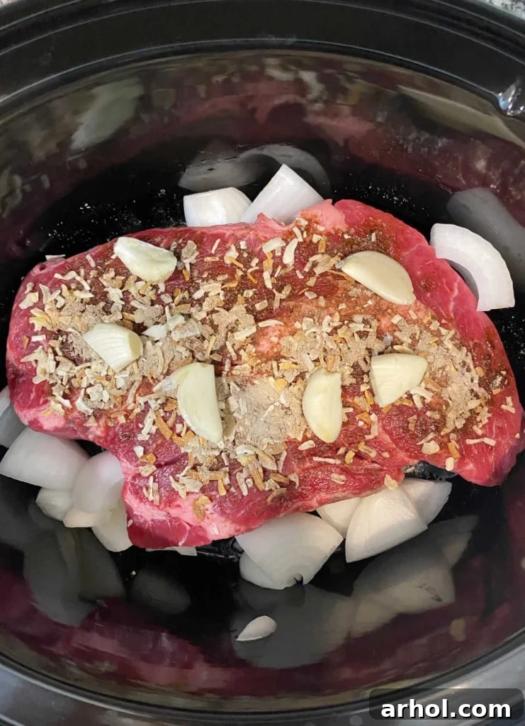 Beef chuck roast with onion soup mix garlic and onions layered in a slow cooker.