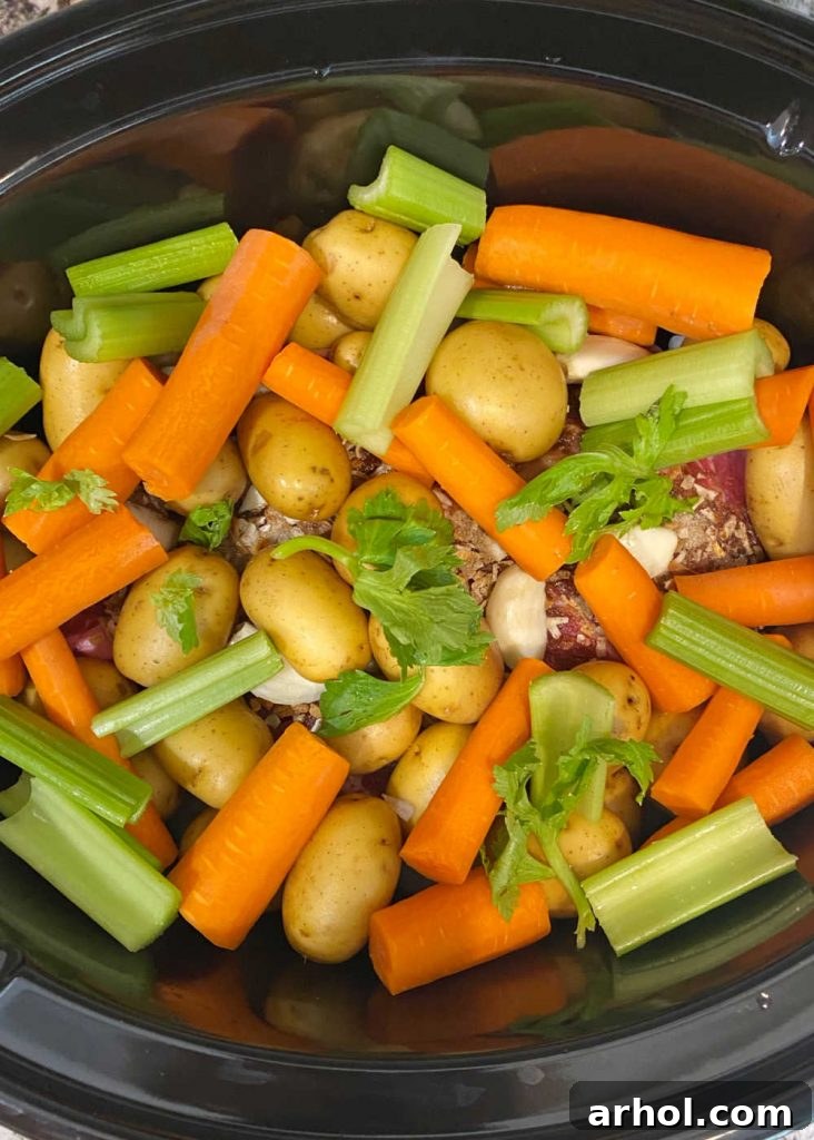 Pot roast with carrots, potatoes, and celery added on top of the beef in the slow cooker.