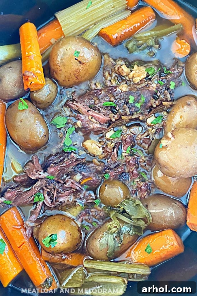 Slow cooker pot roast with tender beef, potatoes, carrots, and celery simmering in rich beef broth.