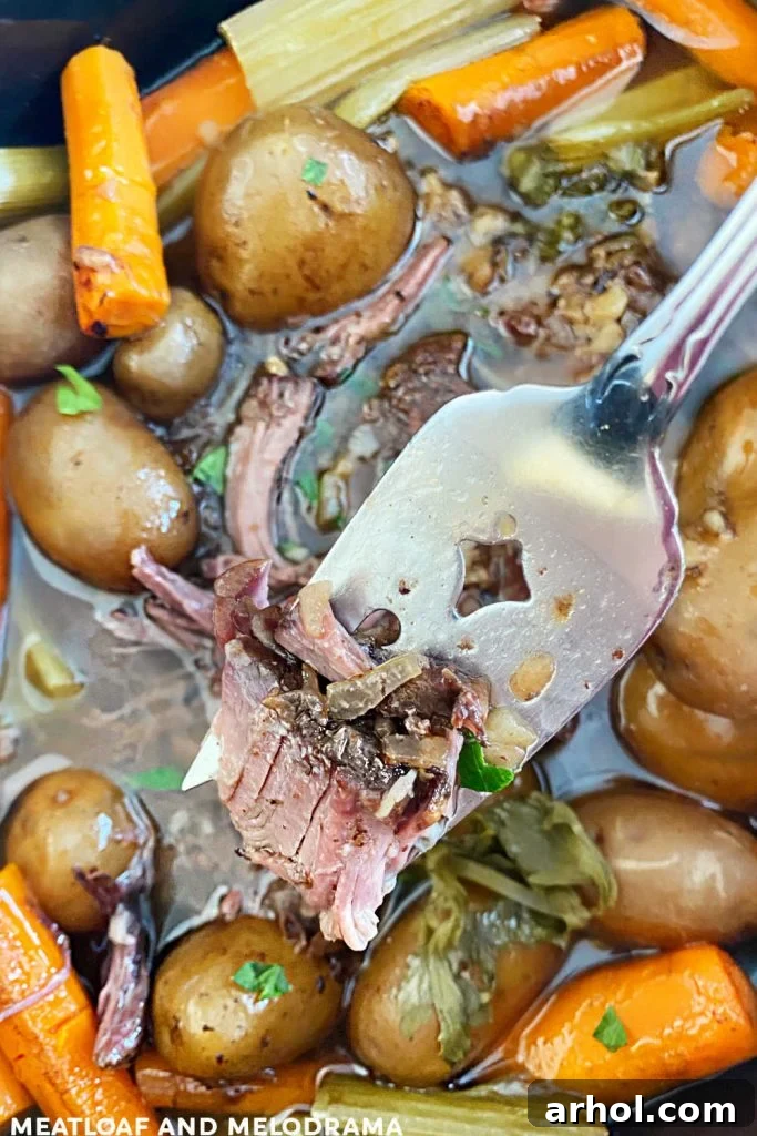 Tender chuck roast being pulled apart with a serving fork, showing its fall-apart texture.