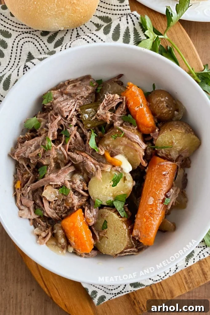 Chuck roast with potatoes and carrots in a white serving bowl, garnished with fresh parsley.