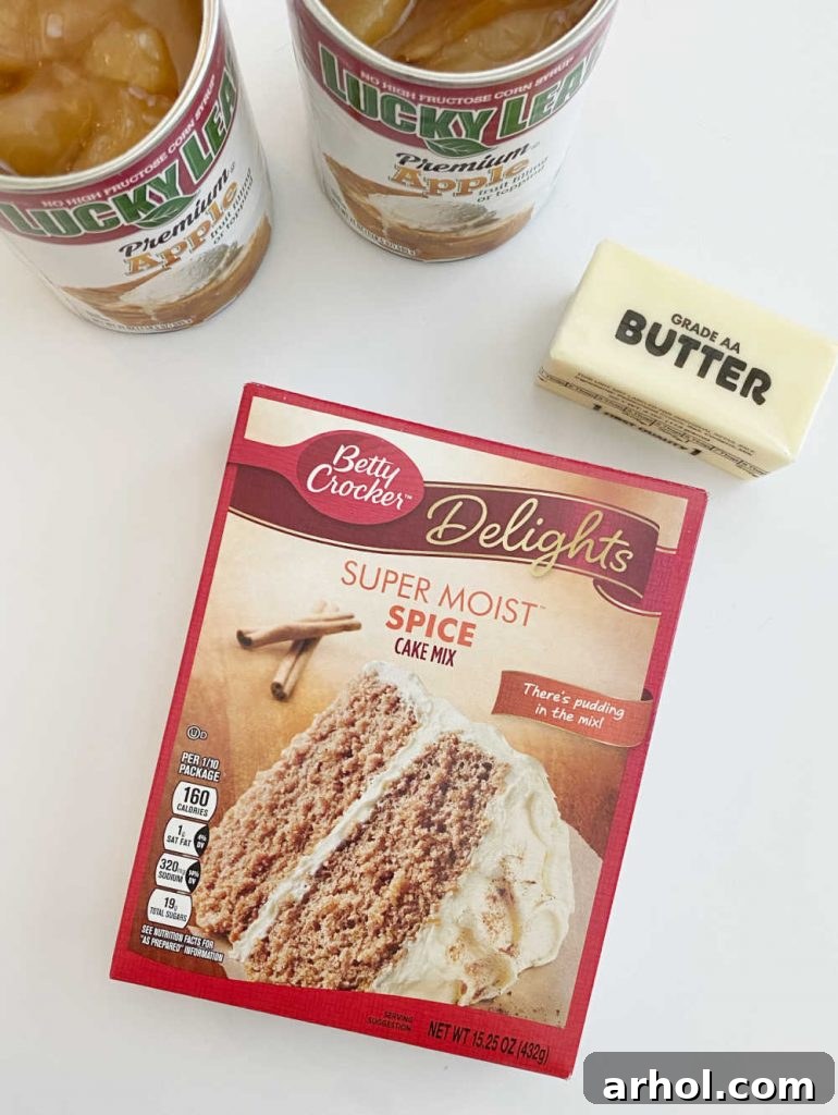Two cans of apple pie filling, a box of spice cake mix, and a stick of butter laid out on a white background.