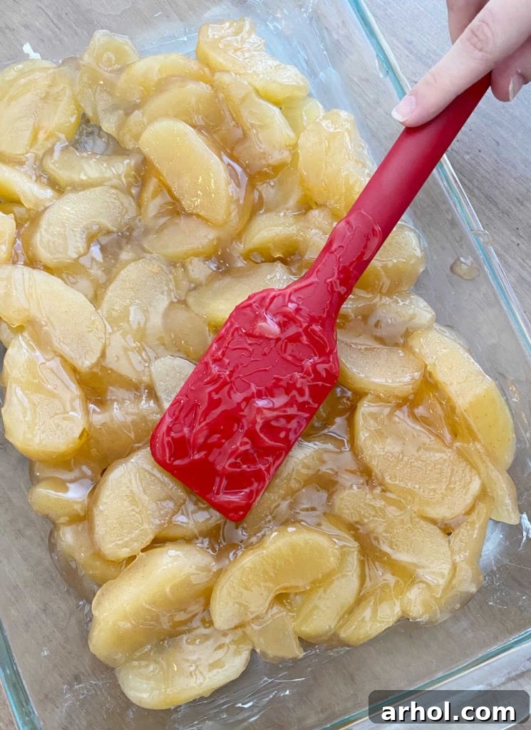 Red spatula spreading apple pie filling evenly into a glass baking dish.