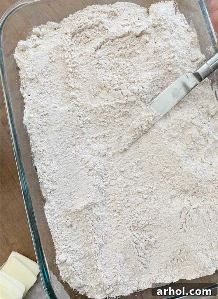 Knife spreading dry spice cake mix evenly over a layer of apple pie filling in a baking dish.