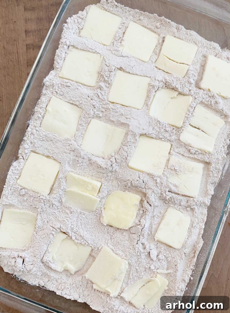 Evenly spaced squares of butter arranged over a layer of spice cake mix in a baking dish, ready for the oven.