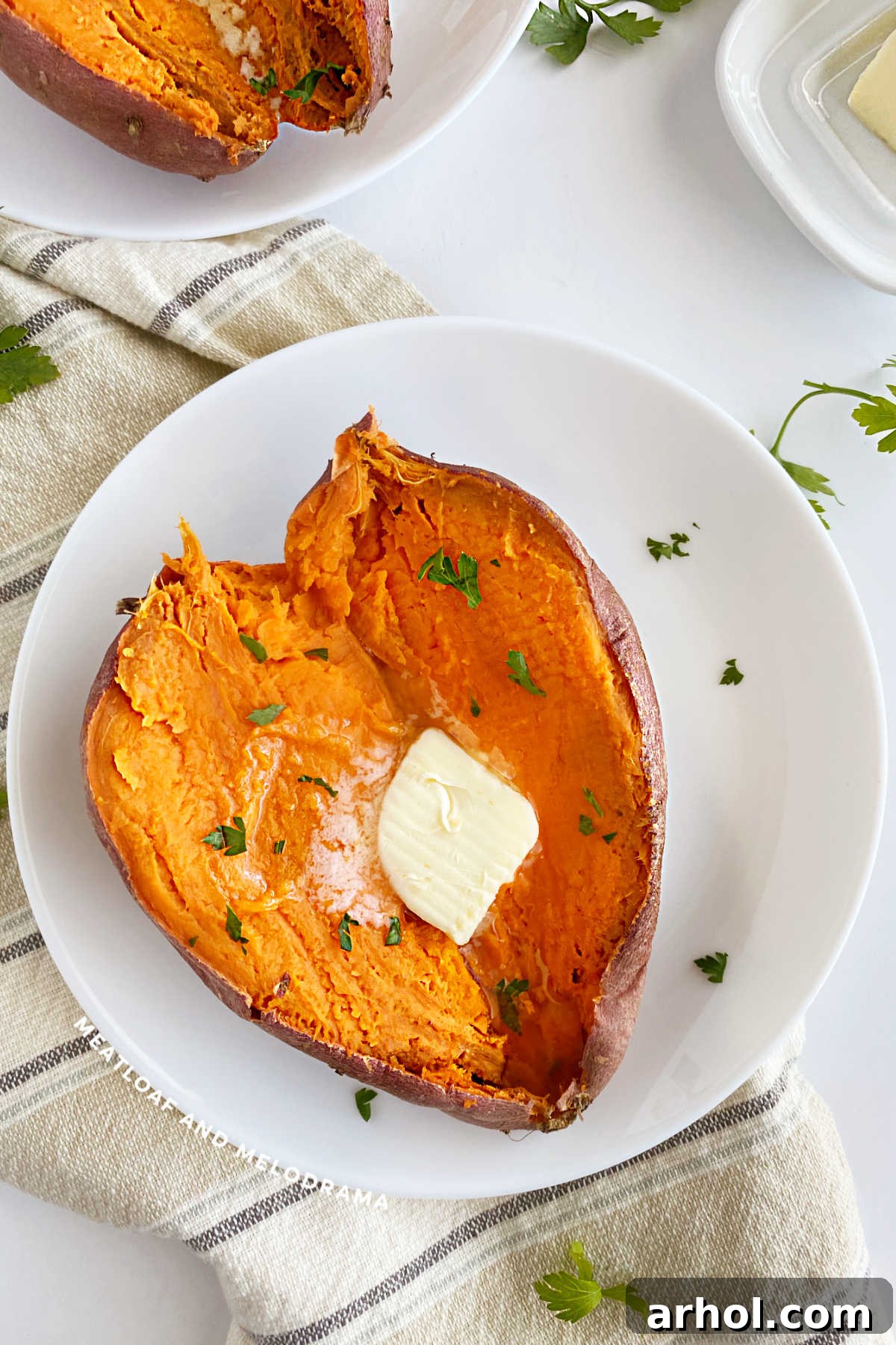 Microwave Sweet Potato in Minutes 2 Microwave sweet potato cut open with a pat of butter and parsley on a plate, ready to eat