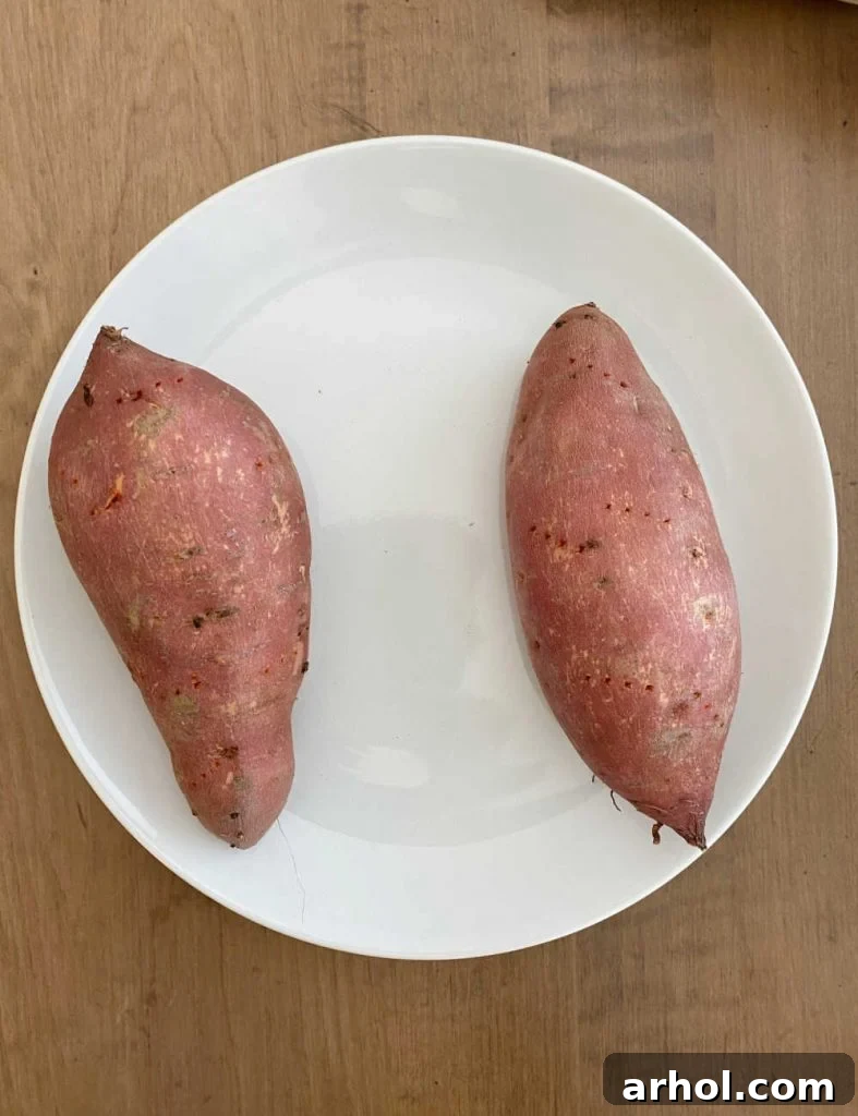 Microwave Sweet Potato in Minutes 5 Two sweet potatoes with fork holes arranged on a white plate, ready for microwaving