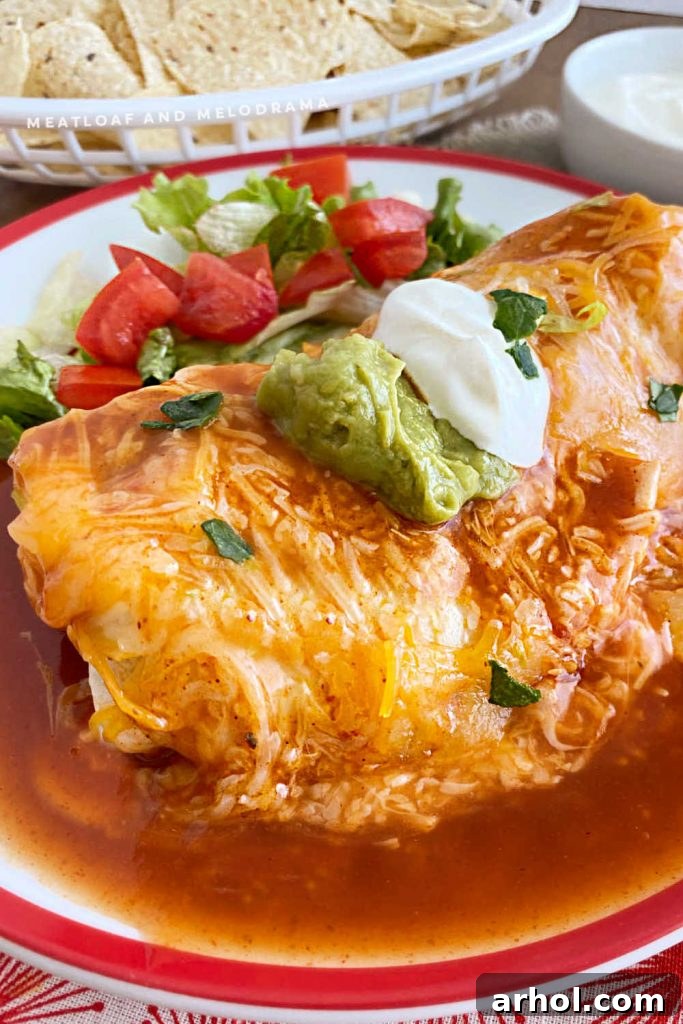 A delicious wet burrito generously smothered in vibrant red enchilada sauce and melted cheddar cheese, served on a white plate, ready to be enjoyed.