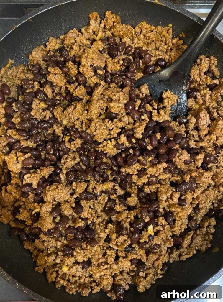 Sautéed ground beef and black beans simmering in a skillet, ready to be used as a delicious filling for wet burritos.