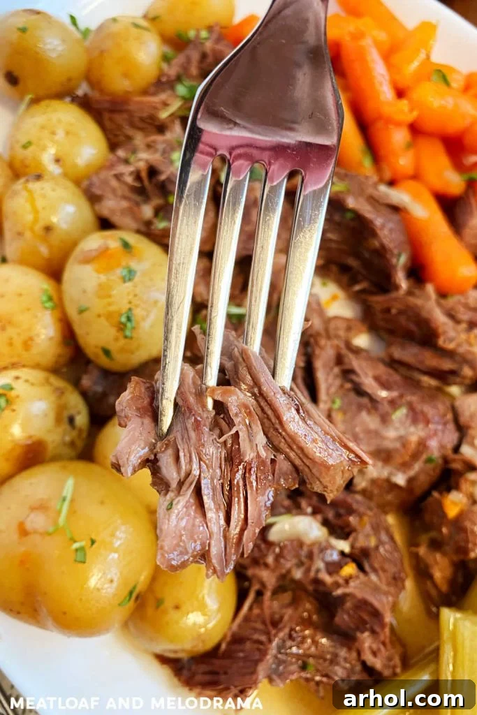 Tender shredded chuck roast on a fork, served with baby potatoes and carrots on a platter