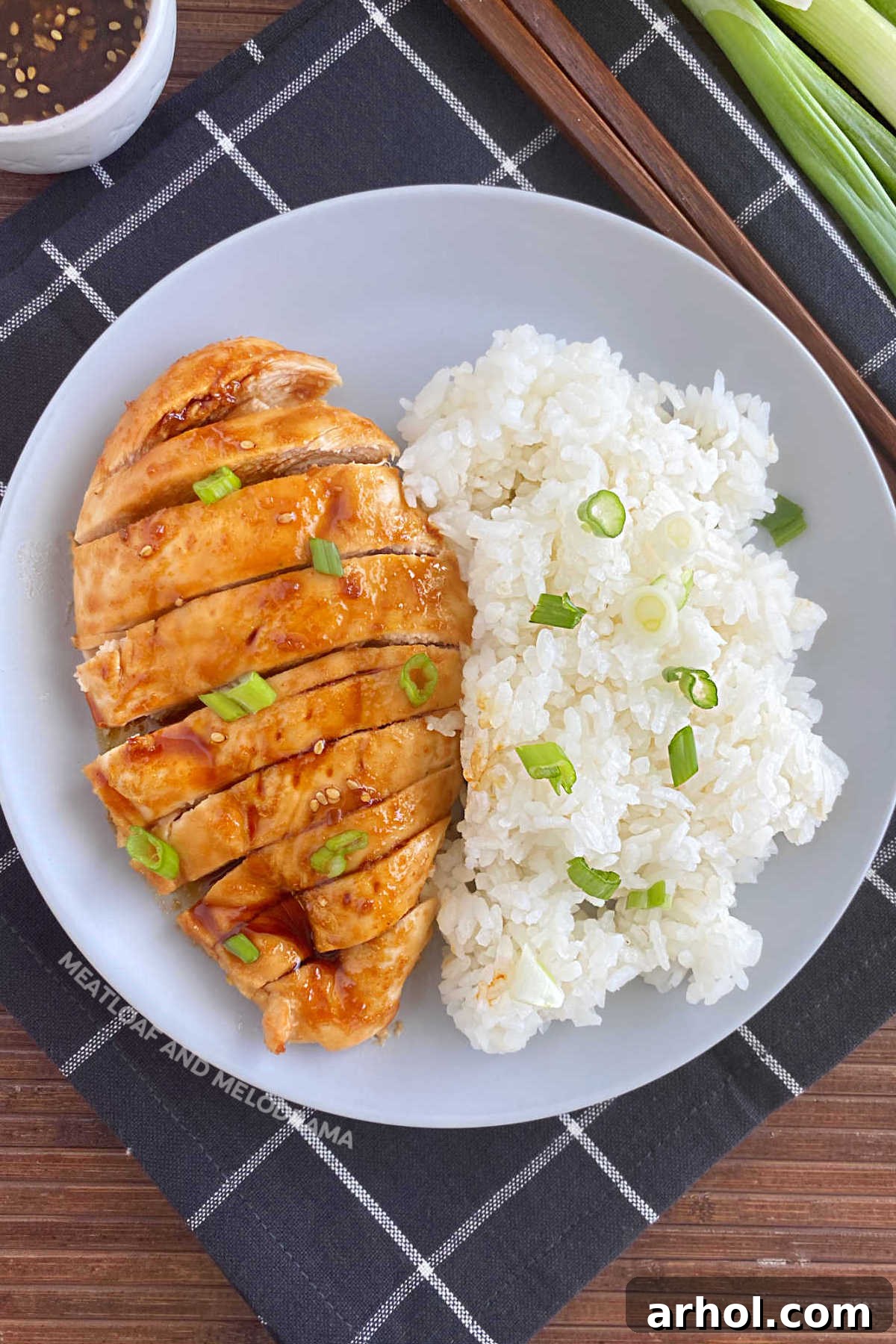 Flavorful baked teriyaki chicken breast, garnished with vibrant green onions, served alongside fluffy white rice on a plate.