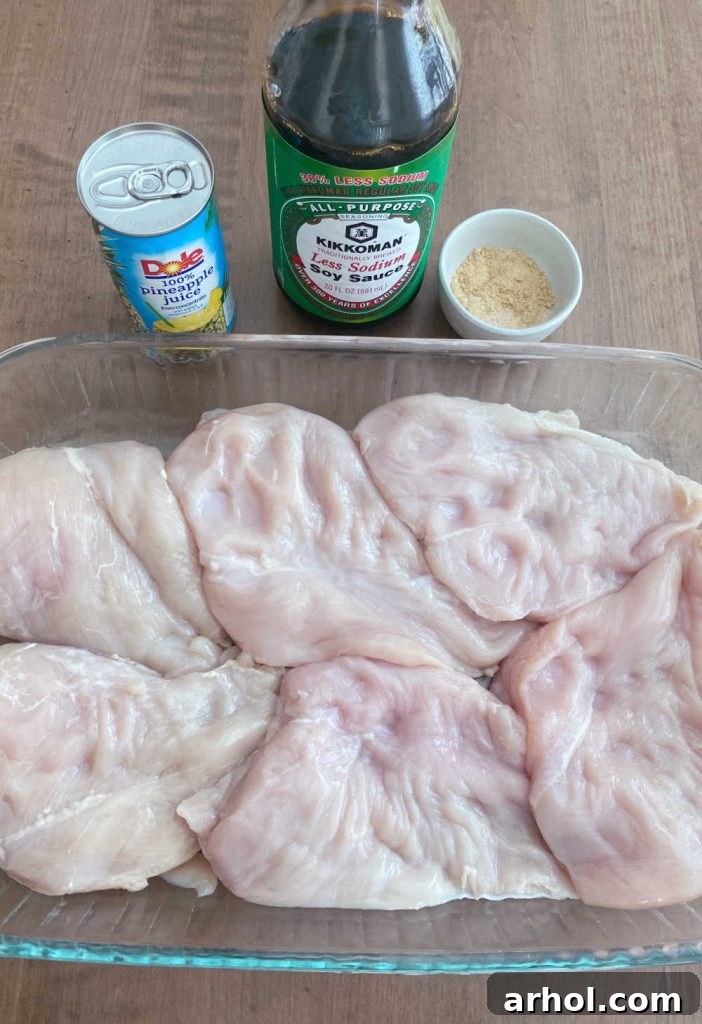 Fresh ingredients laid out: pineapple juice, soy sauce, and raw boneless, skinless chicken breasts on a cutting board, ready for cooking.