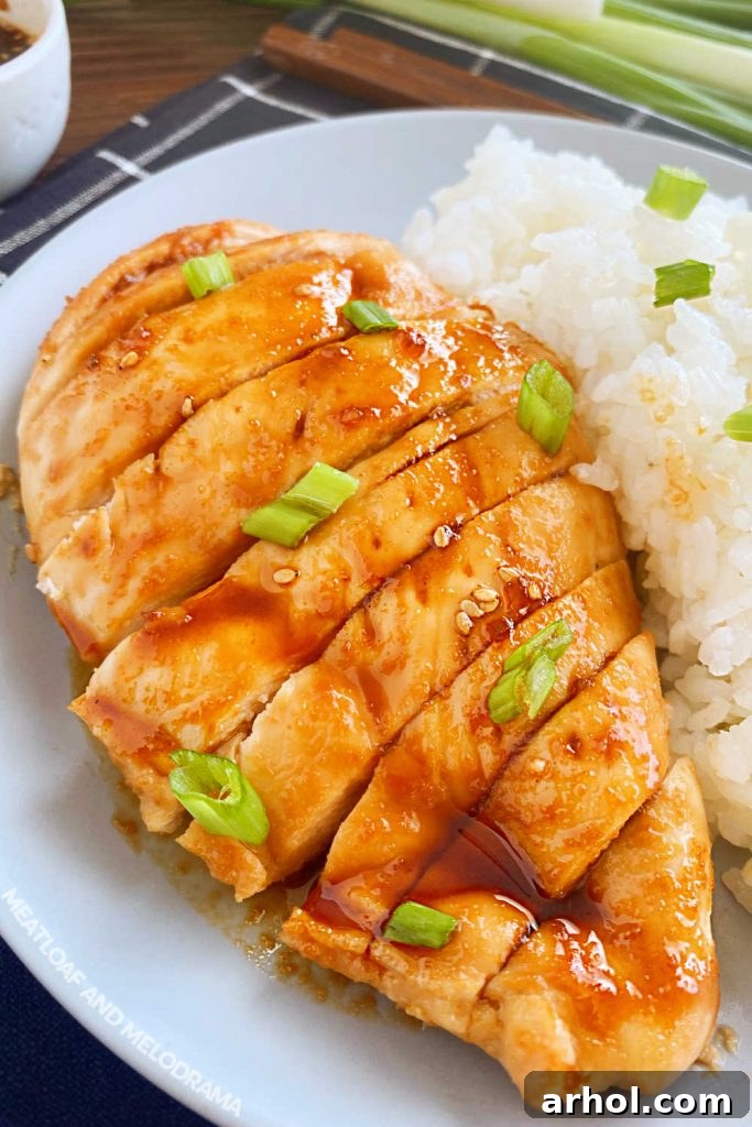 Close-up view of perfectly sliced baked teriyaki chicken breast, adorned with fresh green onions and glistening with homemade sauce.