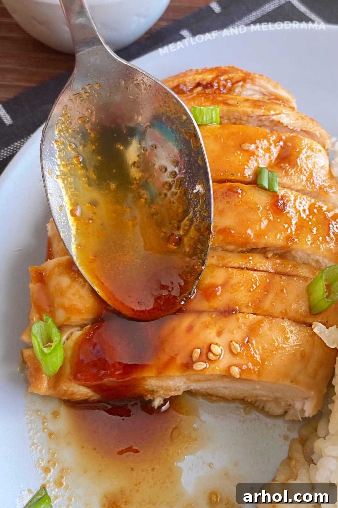 A spoon generously coating sliced baked chicken breast with reduced, thick teriyaki sauce.
