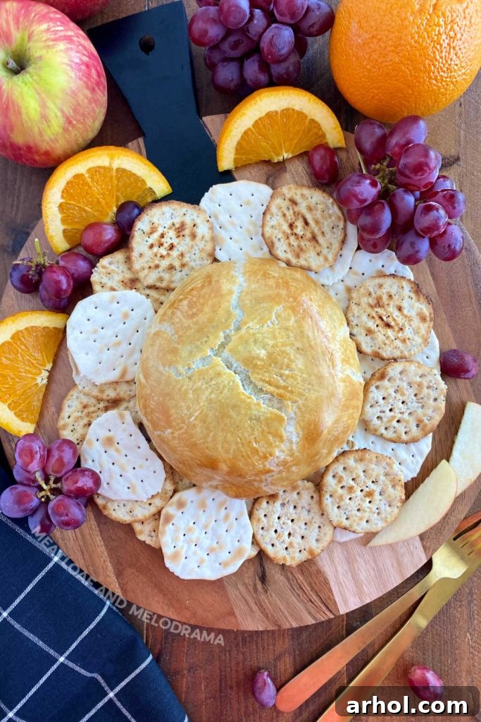 Golden baked brie en croute in puff pastry on a rustic bread board, surrounded by fresh fruit and crackers, ready to serve.