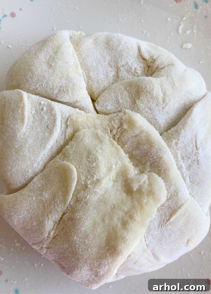 Puff pastry dough being carefully folded over a wheel of brie cheese, topped with jam and cranberries, to create a sealed package.