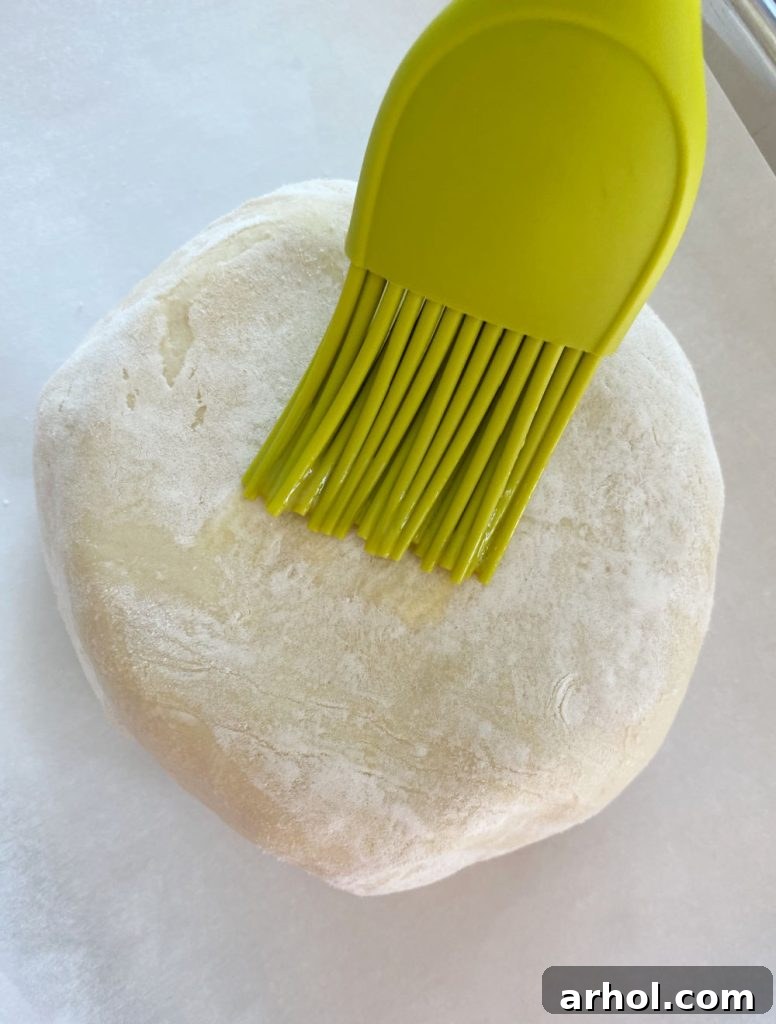 A pastry brush applying egg wash to the surface of the puff pastry wrapped brie, enhancing its golden color before baking.