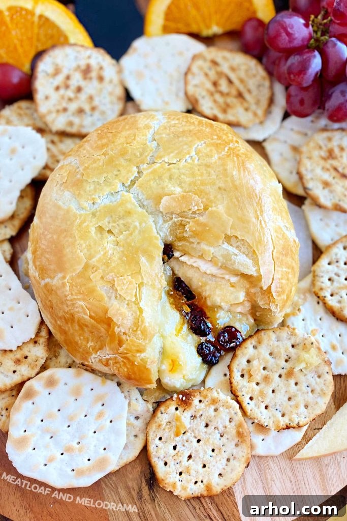 A beautifully baked cranberry brie with orange marmalade in puff pastry, served on a board with an assortment of crackers.