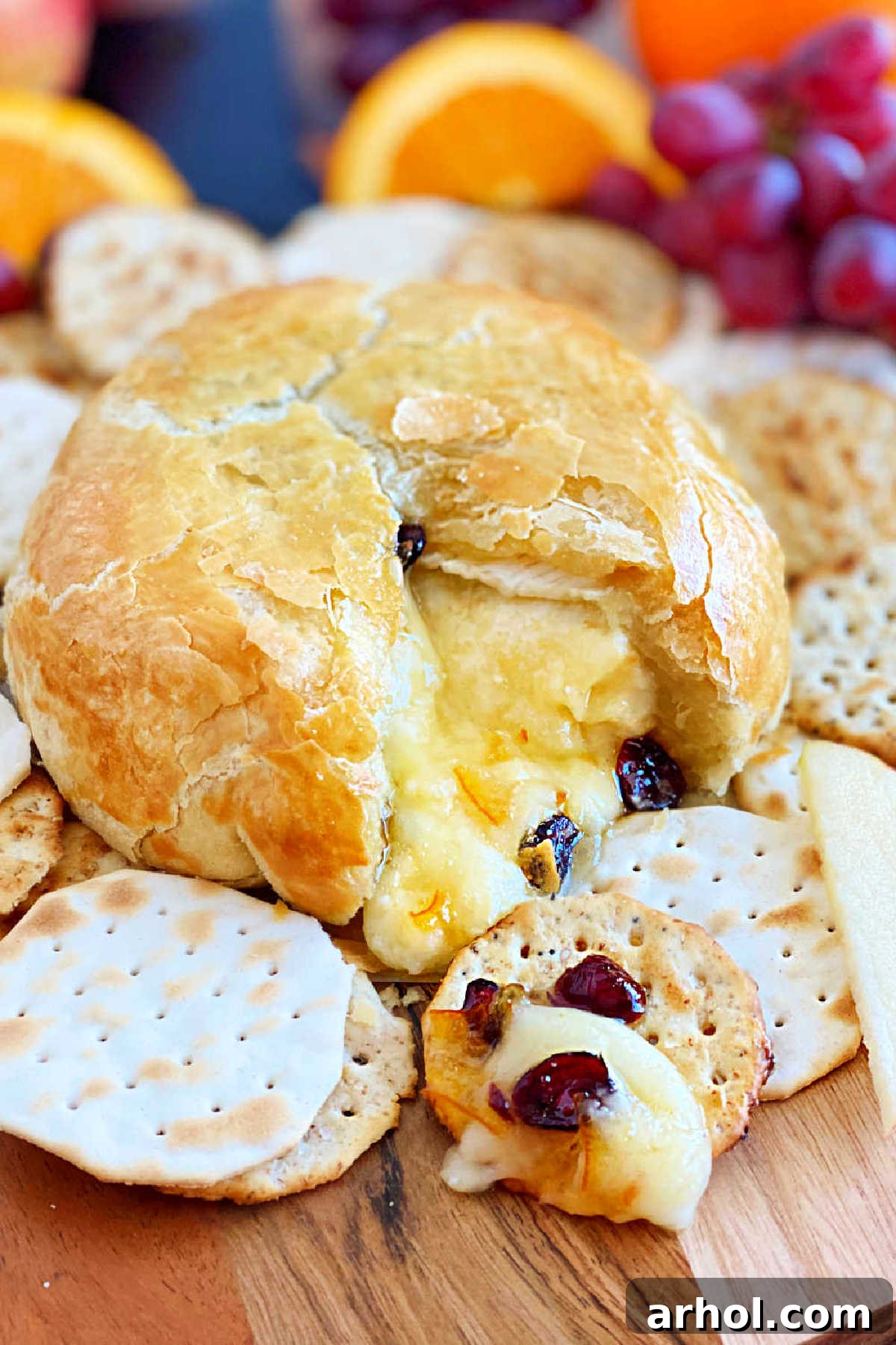 Baked brie in puff pastry, cut open to reveal luscious melted cheese, dried cranberries, and orange marmalade, served with crackers.