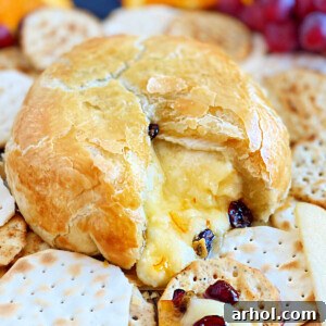 Baked brie cut open with melted cheese, dried cranberries and crackers on a wooden board.