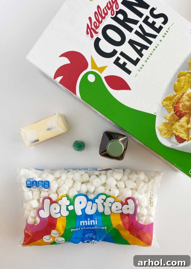 A flat lay showcasing the essential ingredients for Christmas cornflake wreath cookies: Kellogg's Corn Flakes cereal, butter, a bag of mini marshmallows, vanilla extract, and a bottle of green food coloring, all arranged on a rustic wooden table.
