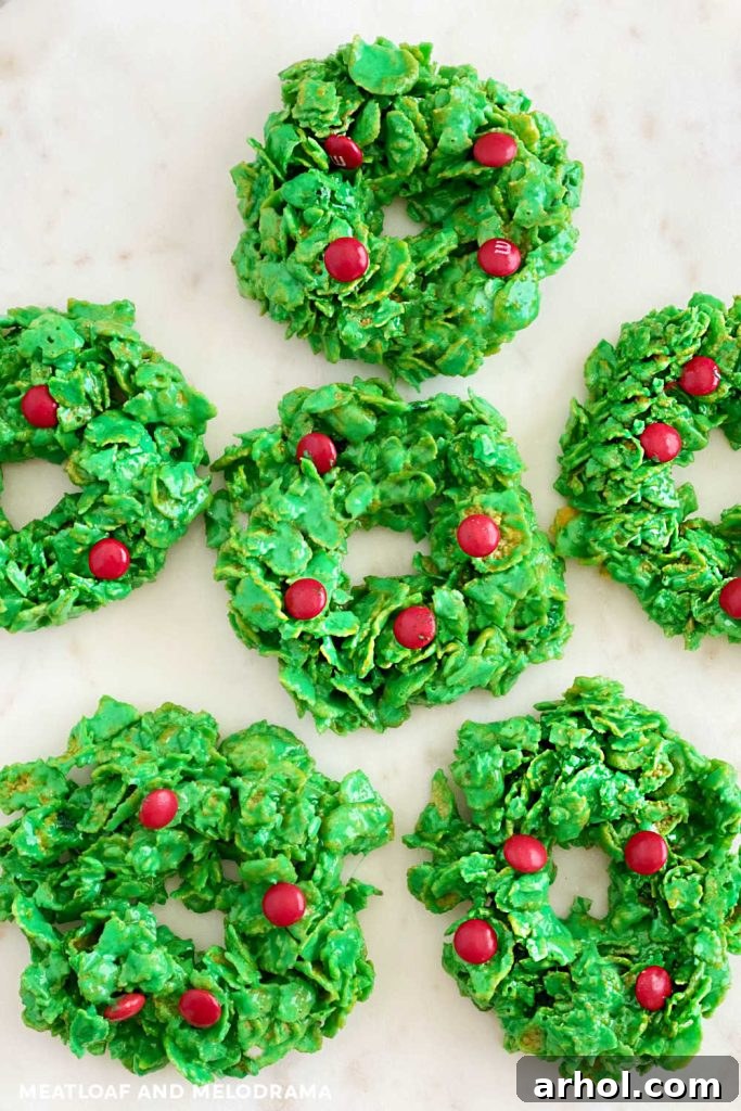 A close-up shot of several vibrant green Christmas cornflake wreath cookies, each decorated with three bright red candies, arranged artfully on a white surface, ready to be a festive treat.