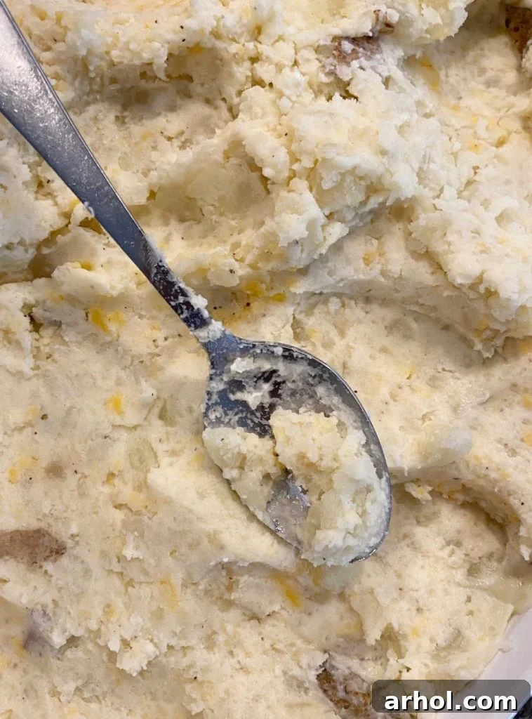 A close-up shot of creamy mashed potato mixture being spread evenly into a buttered baking dish with a large spoon, ready for the final toppings.
