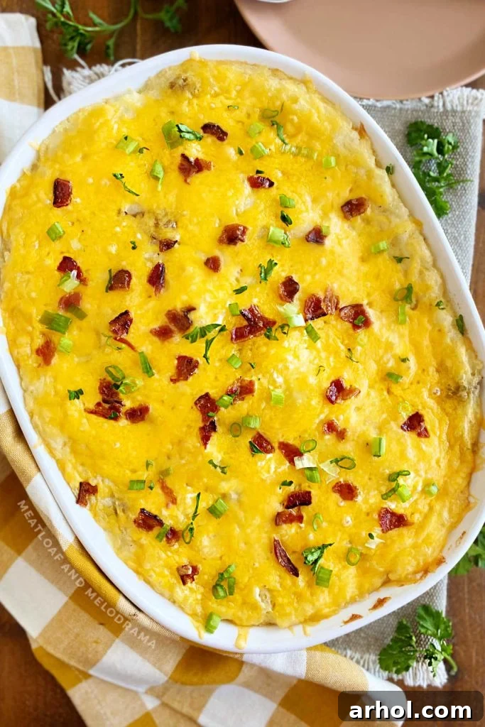 The finished twice baked mashed potatoes casserole, golden and bubbly with melted cheddar and crispy bacon, garnished with fresh green onions, sitting on a table ready for serving.
