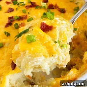 A serving spoon lifting a portion of twice baked potatoes casserole topped with golden cheddar cheese and crispy bacon, garnished with fresh green onions.
