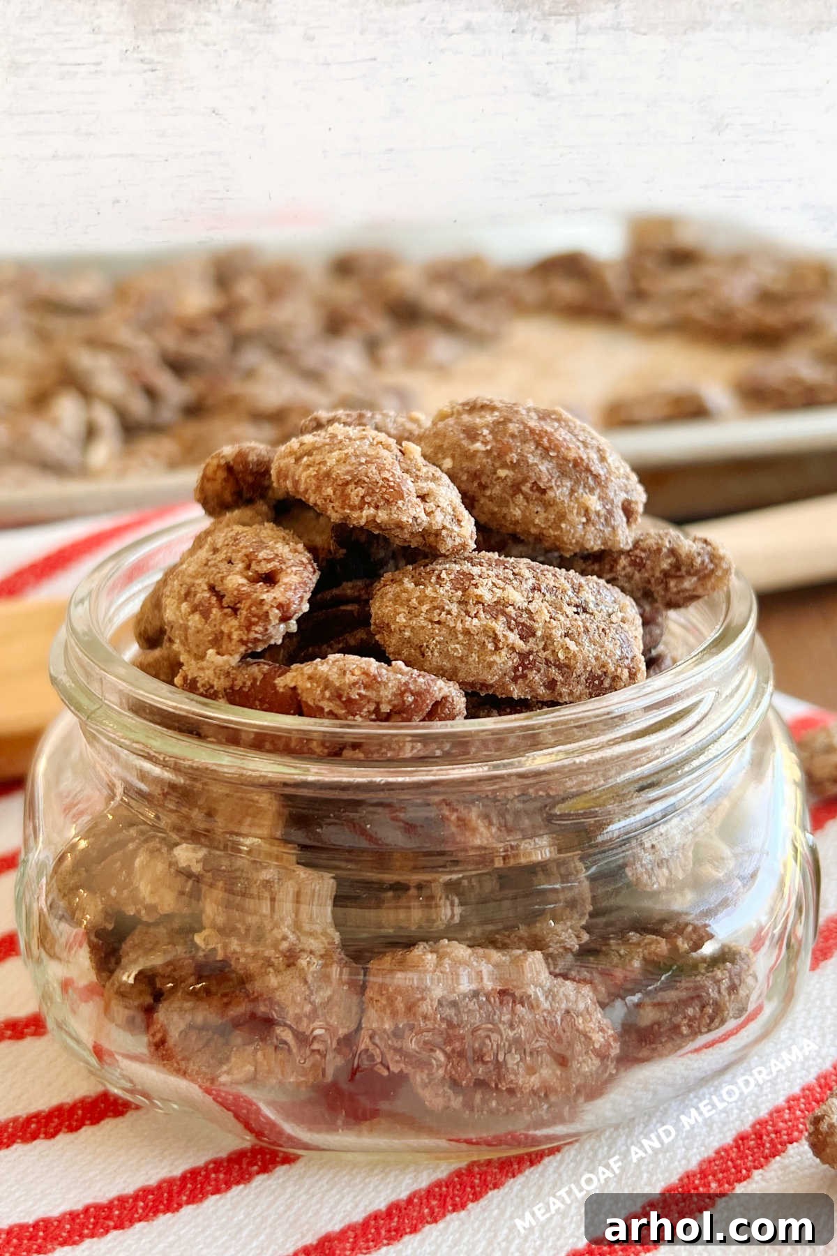 Roasted candied pecans beautifully arranged in a mason jar, placed on a festive red and white towel, ready for gifting or enjoying. This easy candied pecans recipe makes delicious roasted cinnamon sugar pecans in just 20 minutes. Perfect for snacks, holiday gifts, or in salads and desserts. You'll want to make this easy recipe throughout the holiday season!
