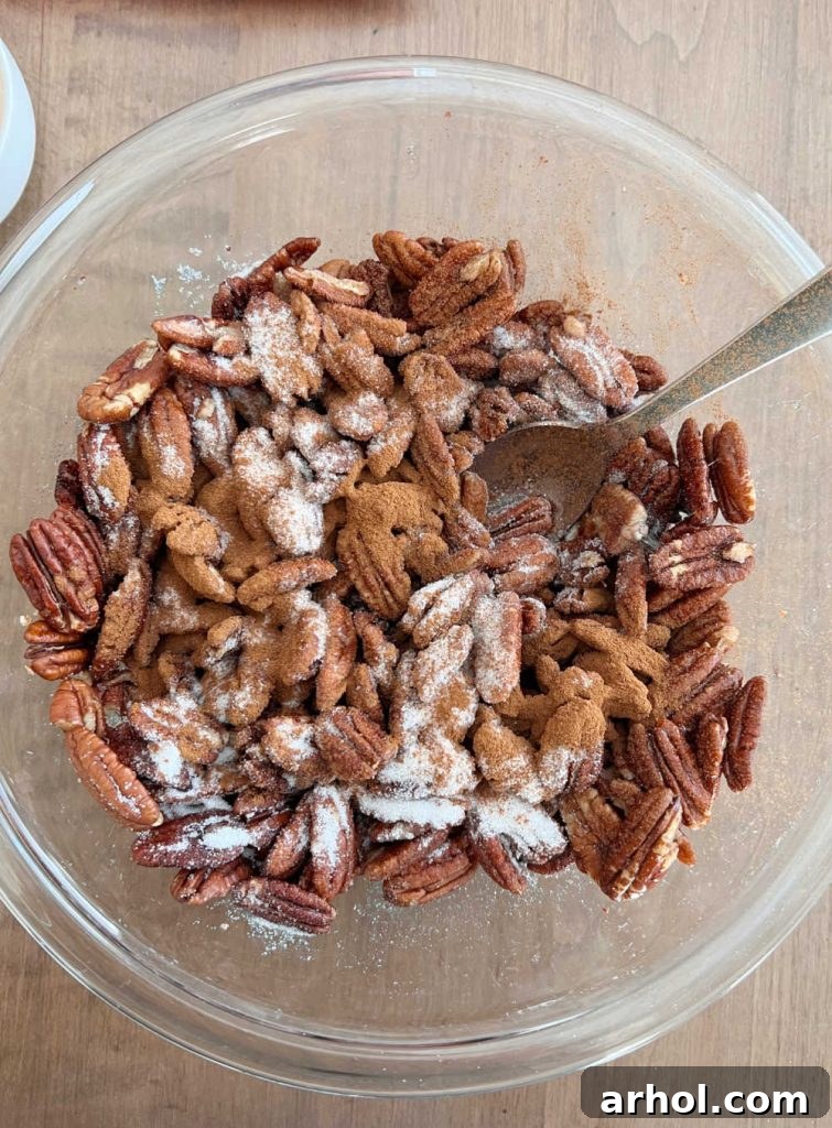 Raw pecan halves tossed with a foamy egg white mixture, cinnamon, and sugar in a large mixing bowl, ready for baking.