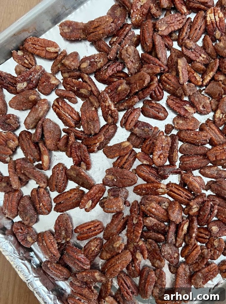Cinnamon sugar coated pecan halves spread evenly in a single layer on a parchment-lined baking sheet, ready to be roasted.