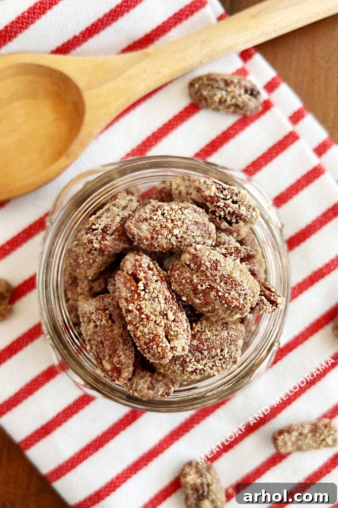Overhead view of homemade candied pecans presented in a rustic mason jar, accompanied by a wooden spoon, perfect for serving or gifting.