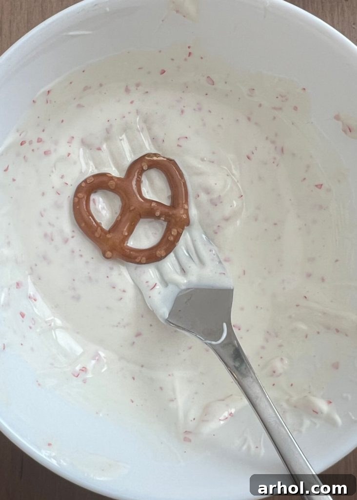 A mini pretzel twist being carefully dipped into a bowl of creamy white chocolate