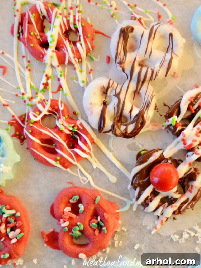 Freshly dipped white chocolate pretzels being decorated with colorful holiday sprinkles on parchment paper