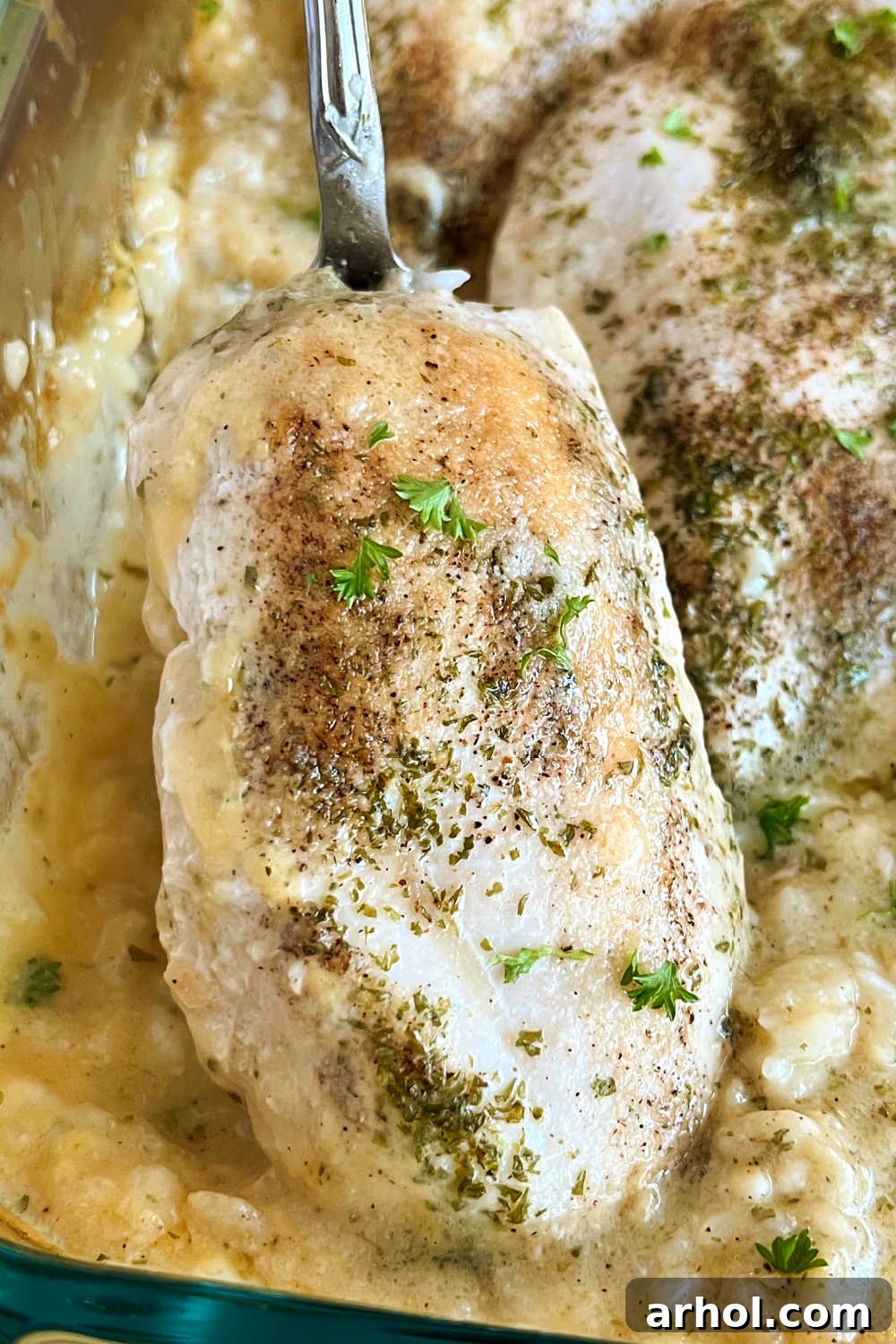 A large serving spoon scooping creamy No Peek Chicken and Rice from a casserole dish, highlighting the tender chicken and fluffy rice.