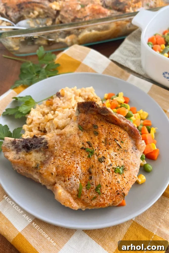 Golden brown baked pork chops and creamy rice served with mixed vegetables on a dinner table, ready to eat.