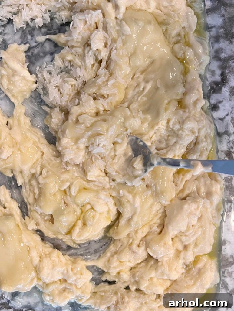 A close-up view of a baking dish where raw jasmine rice, cream of celery soup, cream of onion soup, and melted butter are being stirred together to create the creamy rice base.