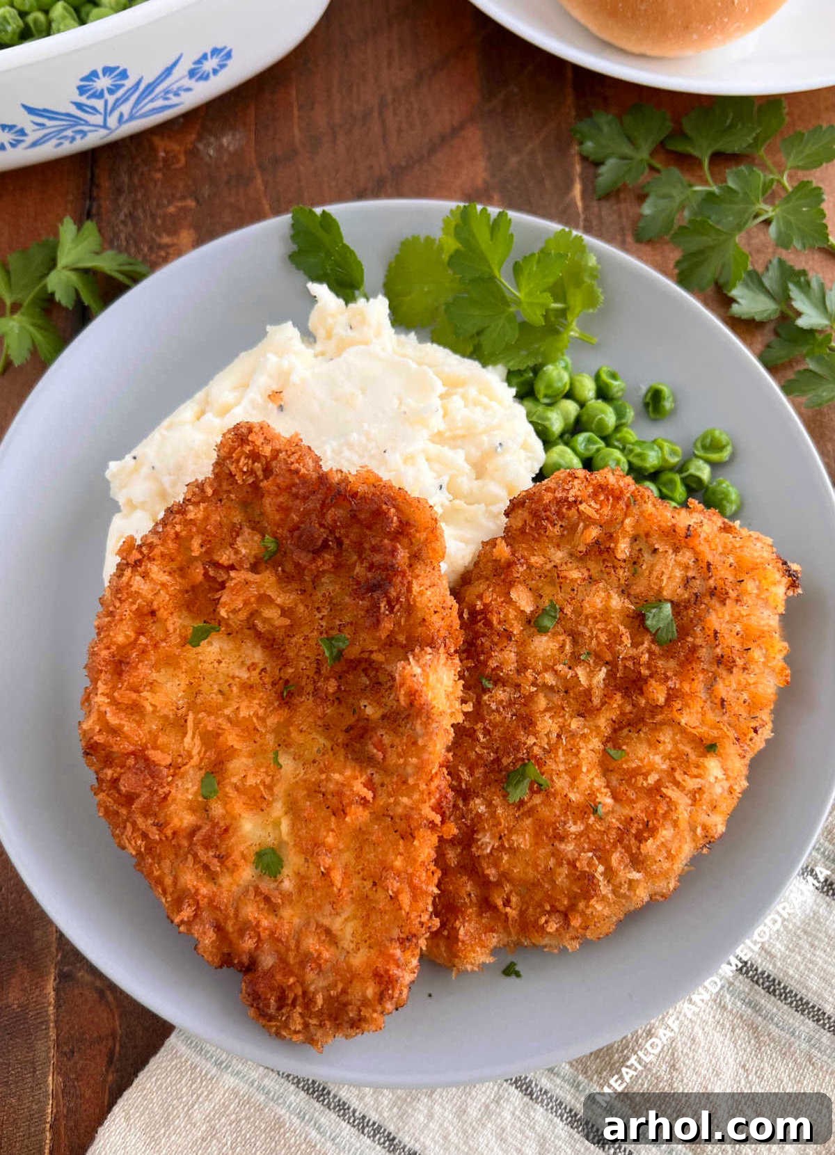 Two crispy Polish breaded pork chops (Kotlet Schabowy) served on a rustic wooden table with traditional side dishes like mashed potatoes and peas.