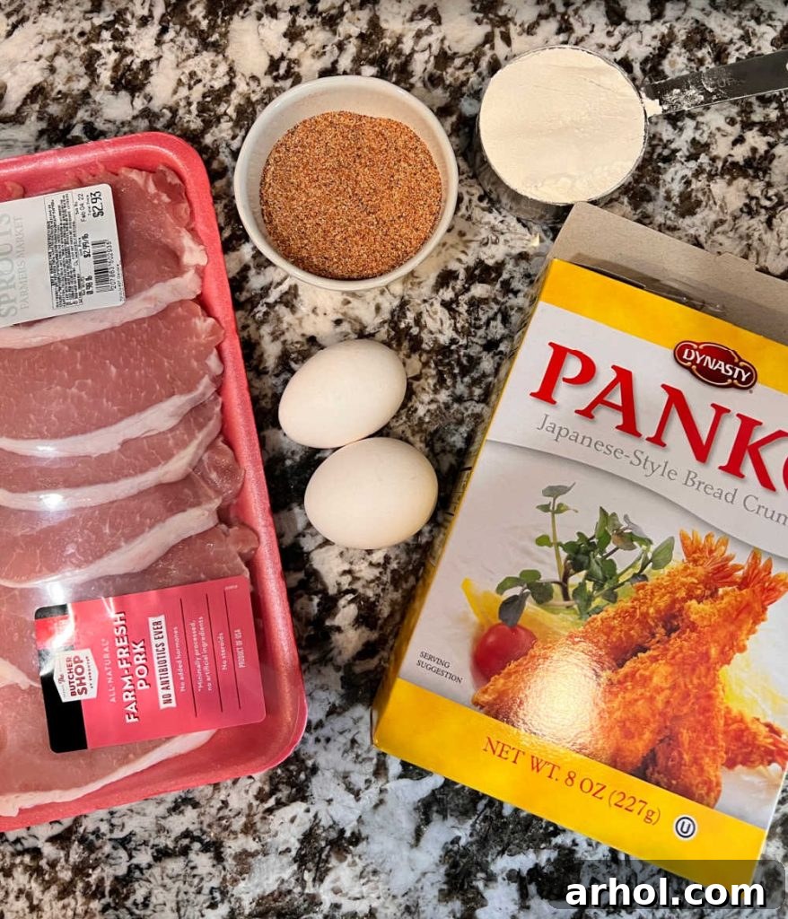 A selection of raw boneless pork cutlets, eggs, various spices (salt, garlic powder, onion powder, black pepper, smoked paprika), all-purpose flour, and Panko breadcrumbs laid out on a kitchen counter, ready for preparing Polish breaded pork chops.