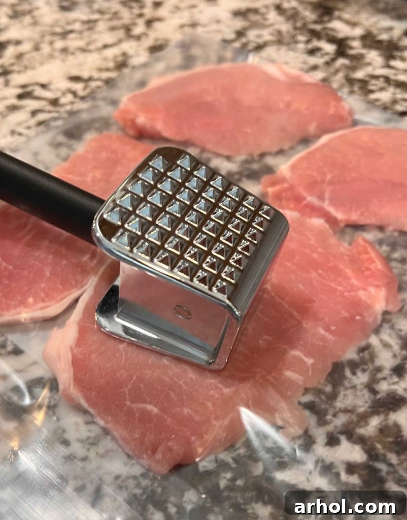 A boneless pork cutlet being pounded thin with a meat mallet inside a clear freezer bag on a cutting board, preparing it for breading.