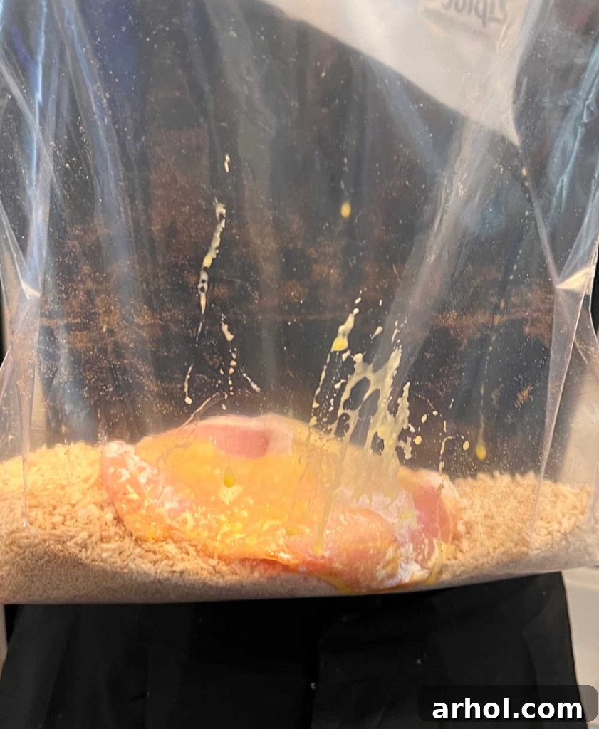 A boneless pork cutlet, coated in egg, being placed into a zip-top bag filled with seasoned breadcrumbs, ready for its final coating.