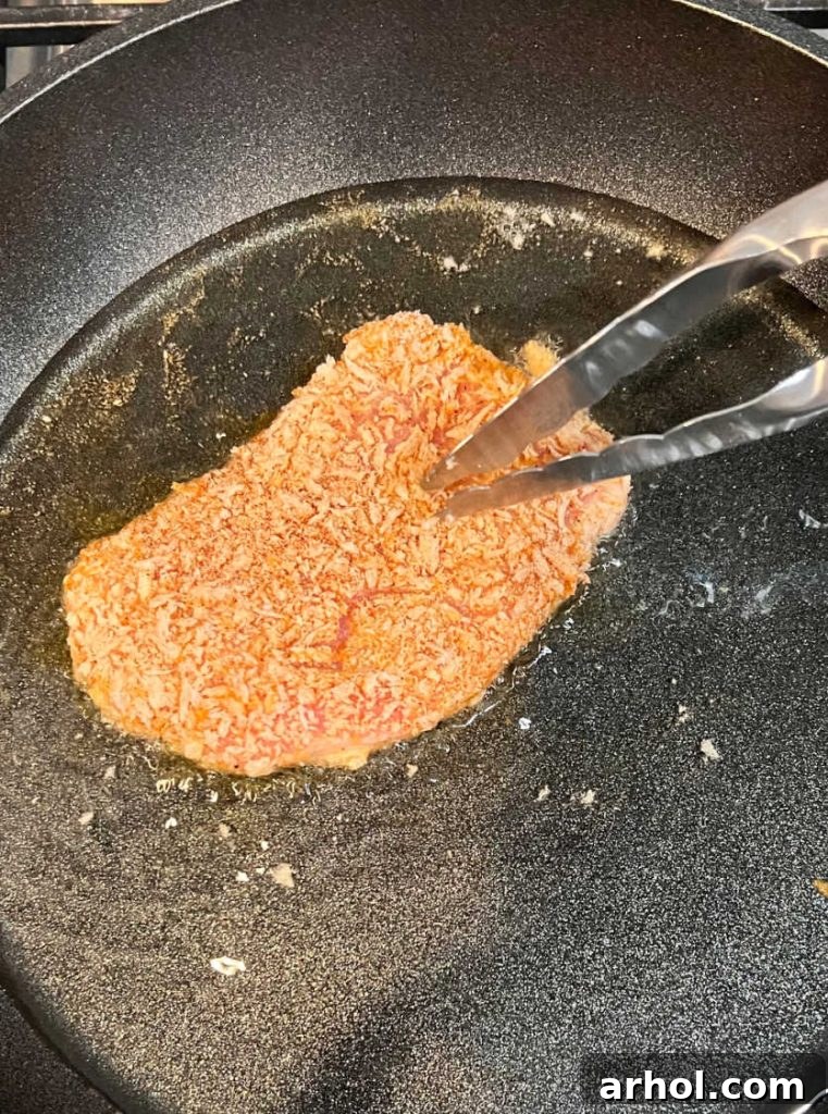 A breaded Polish pork cutlet sizzling in hot oil in a frying pan on a stove, achieving a perfect golden brown crust.