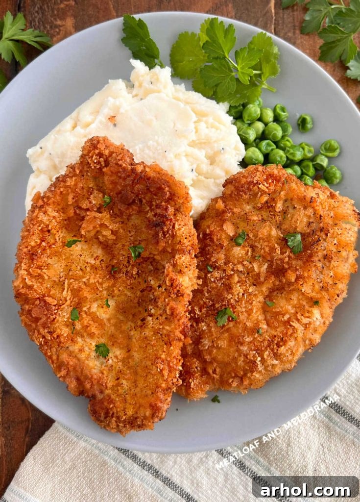 Two golden-brown Polish breaded pork chops (Kotlet Schabowy) served on a white plate with creamy mashed potatoes and green peas, ready to be enjoyed.
